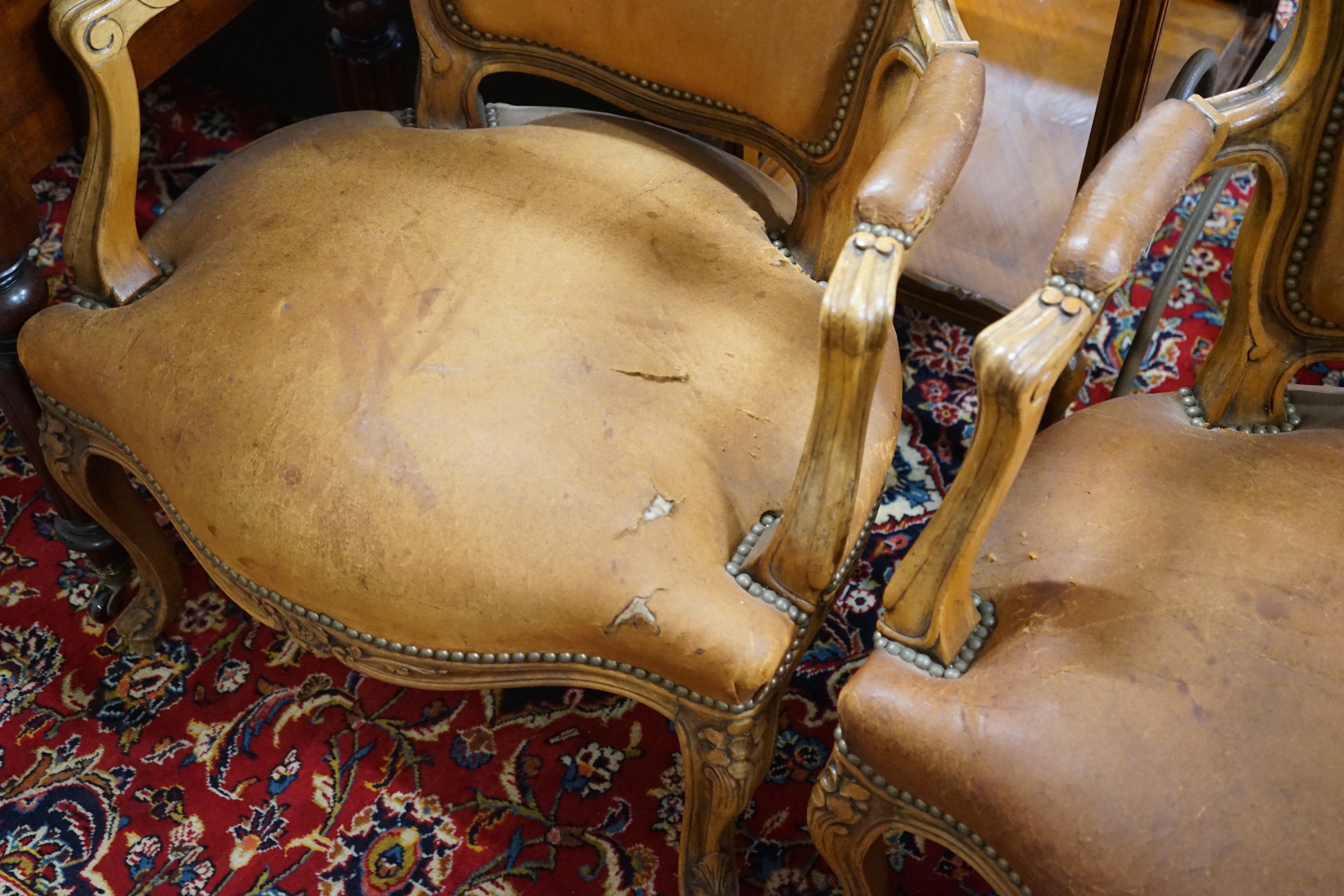 A pair of Louis XVI style carved walnut and tan leather fauteuils, width 62cm, depth 55cm, height 88cm